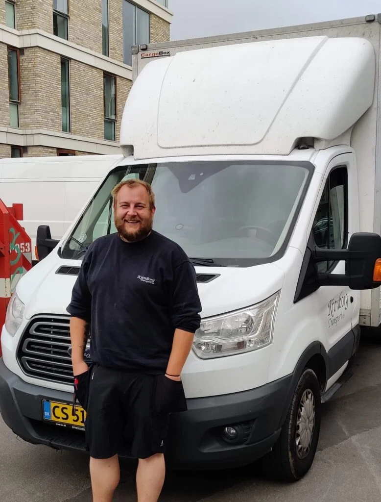Mand smiler foran hvid varevogn i byen.