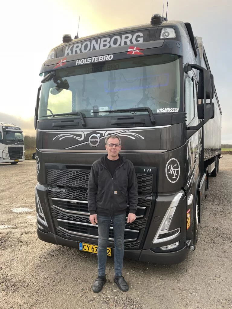 Chauffør står foran stor lastbil på parkeringsplads.