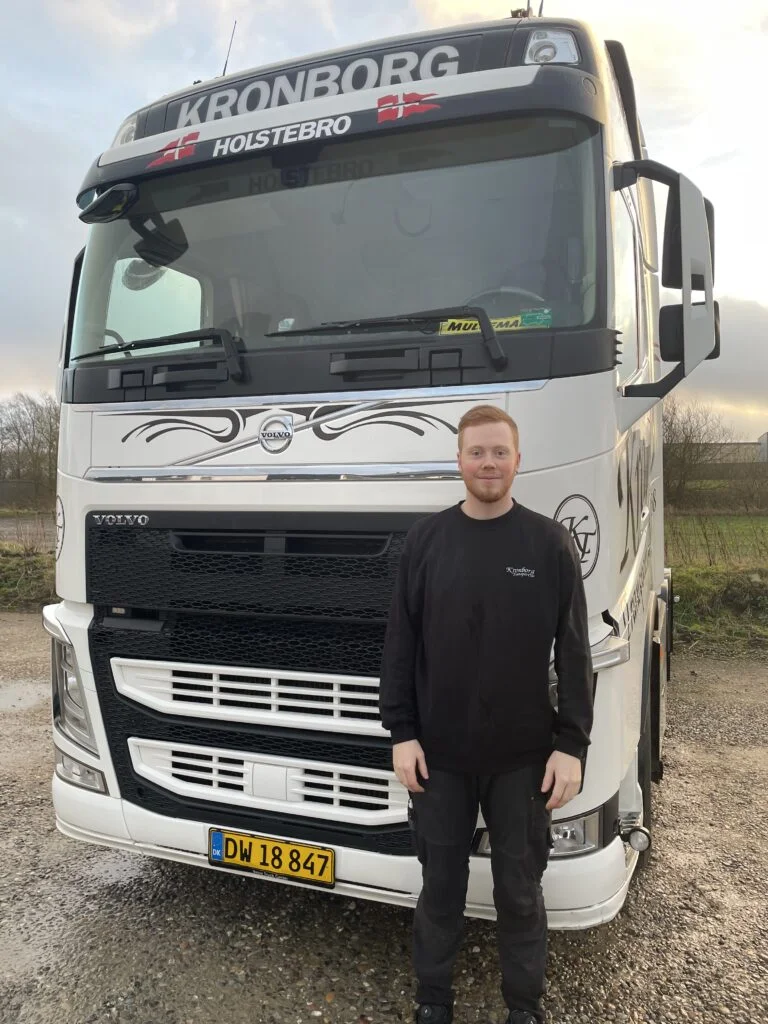 Mand står foran lastbil med nummerplade.