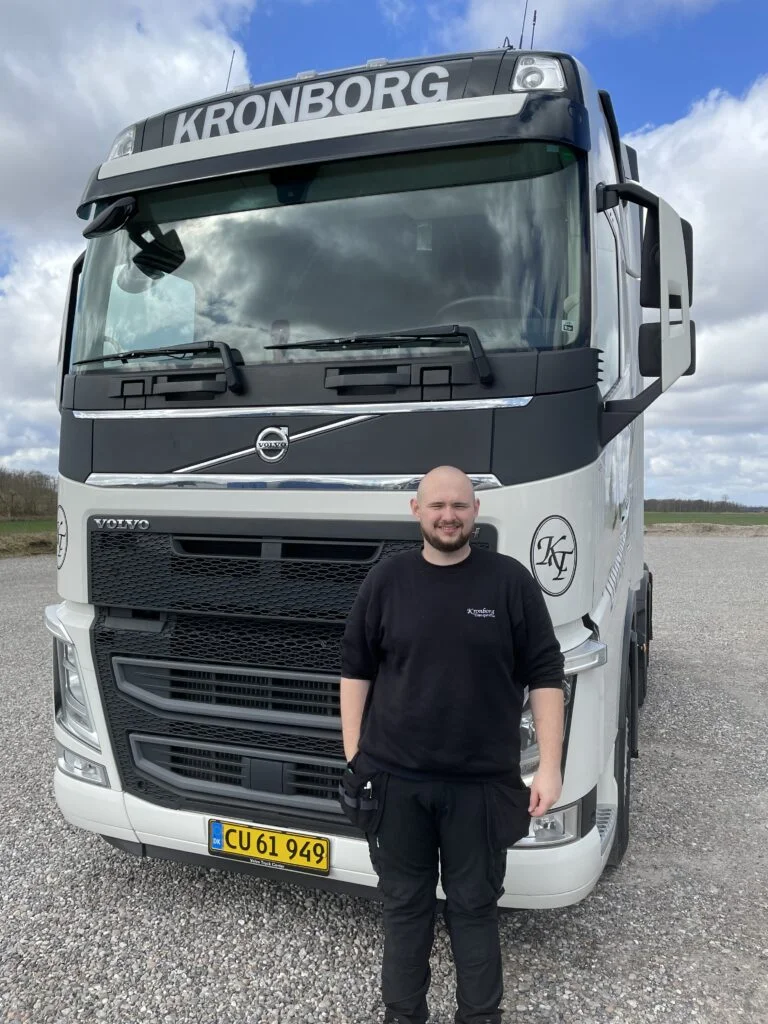 Chauffør foran stor hvid lastbil på parkeringsplads.