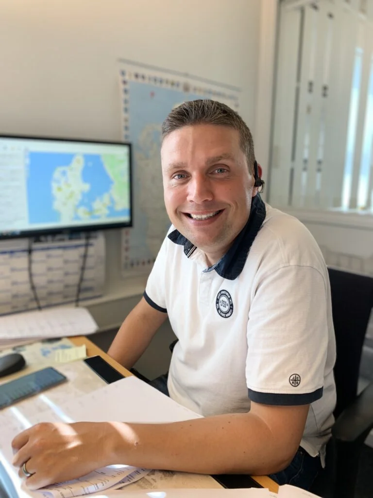 Mand ved skrivebord smiler foran computerskærm med kort.